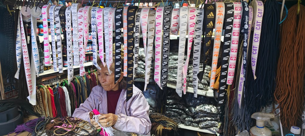 Old Peruvian lady in footwear market with footwear tongue labels in rolls above her head