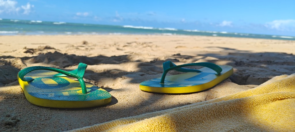 Havianas on beach low-down camera angle with beach towel in foreground and sea in background