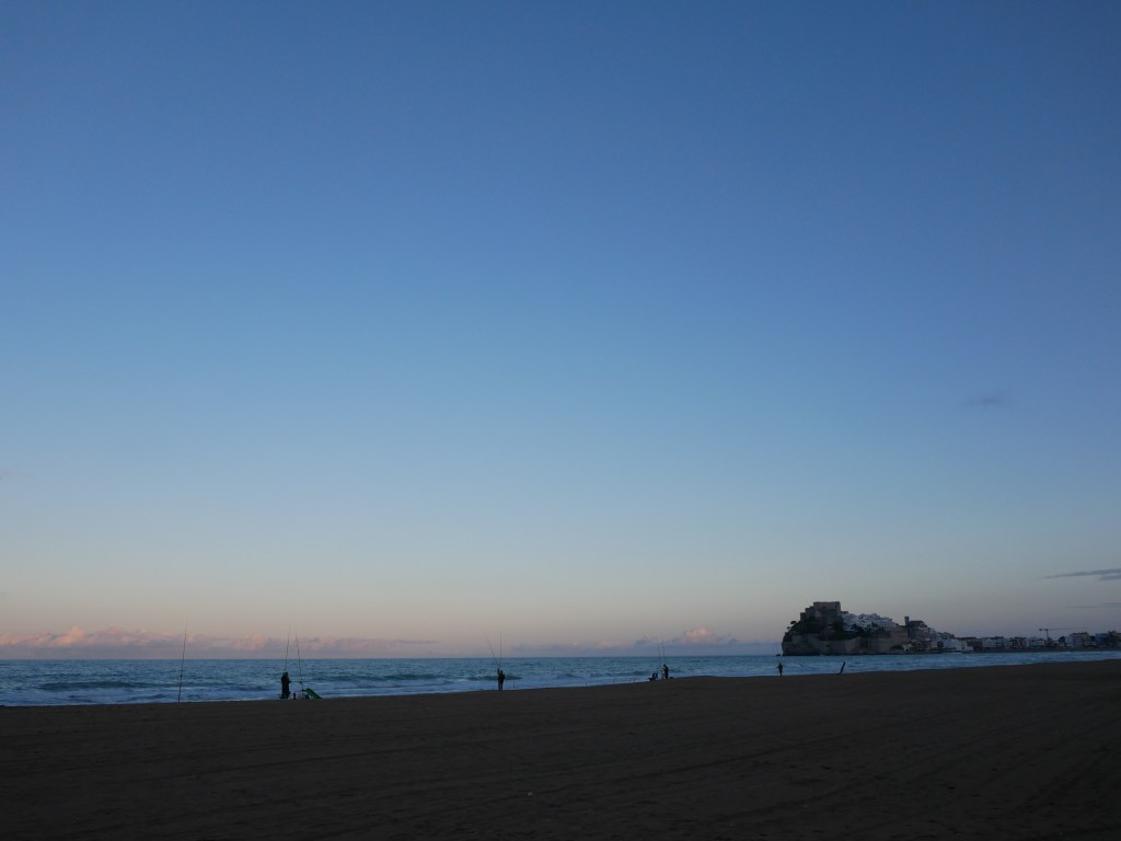 fisherman lined up on beach on an evening in peniscola spain sunset with castle in the background